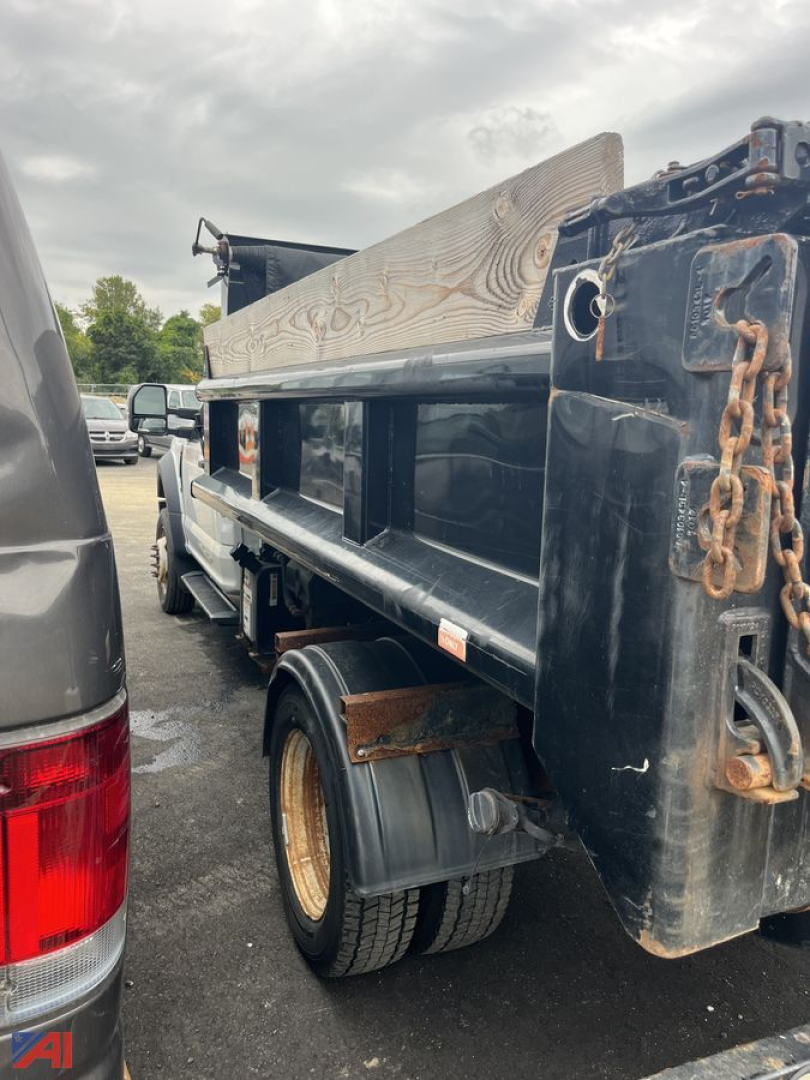 Ford F-550 dump truck bed with chain and wooden side panel, dual rear wheels, visible rear wheel and hydraulic dump bed structure.