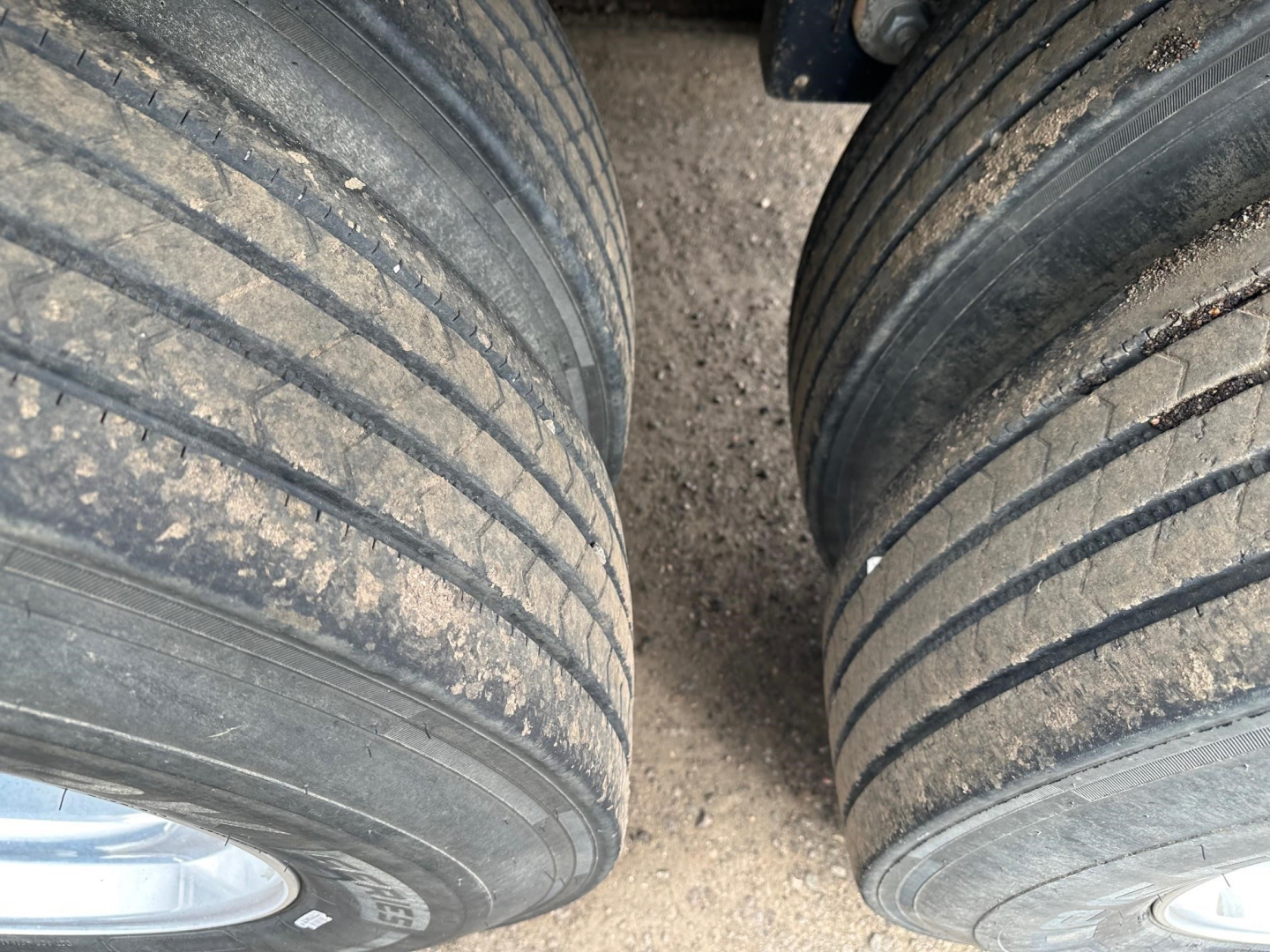 Timpte Super Hopper trailer tires and mud on tread with dual wheels visible, left and right wheels with rims, surface dust.