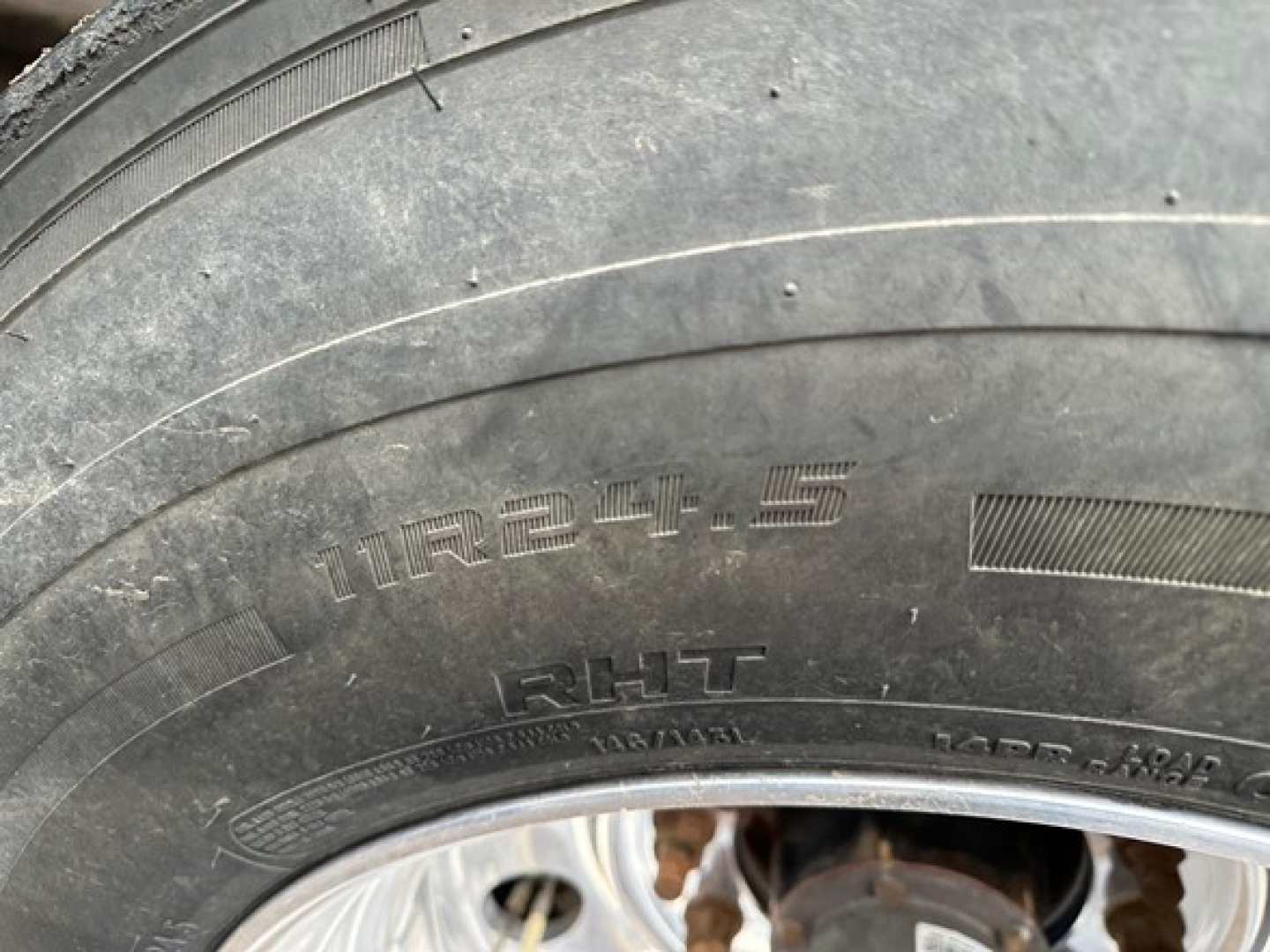 Tire close-up on a 2024 Timpte Super Hopper trailer showing the tire size 11R24.5 and rim hub area with visible rust on undercarriage components.