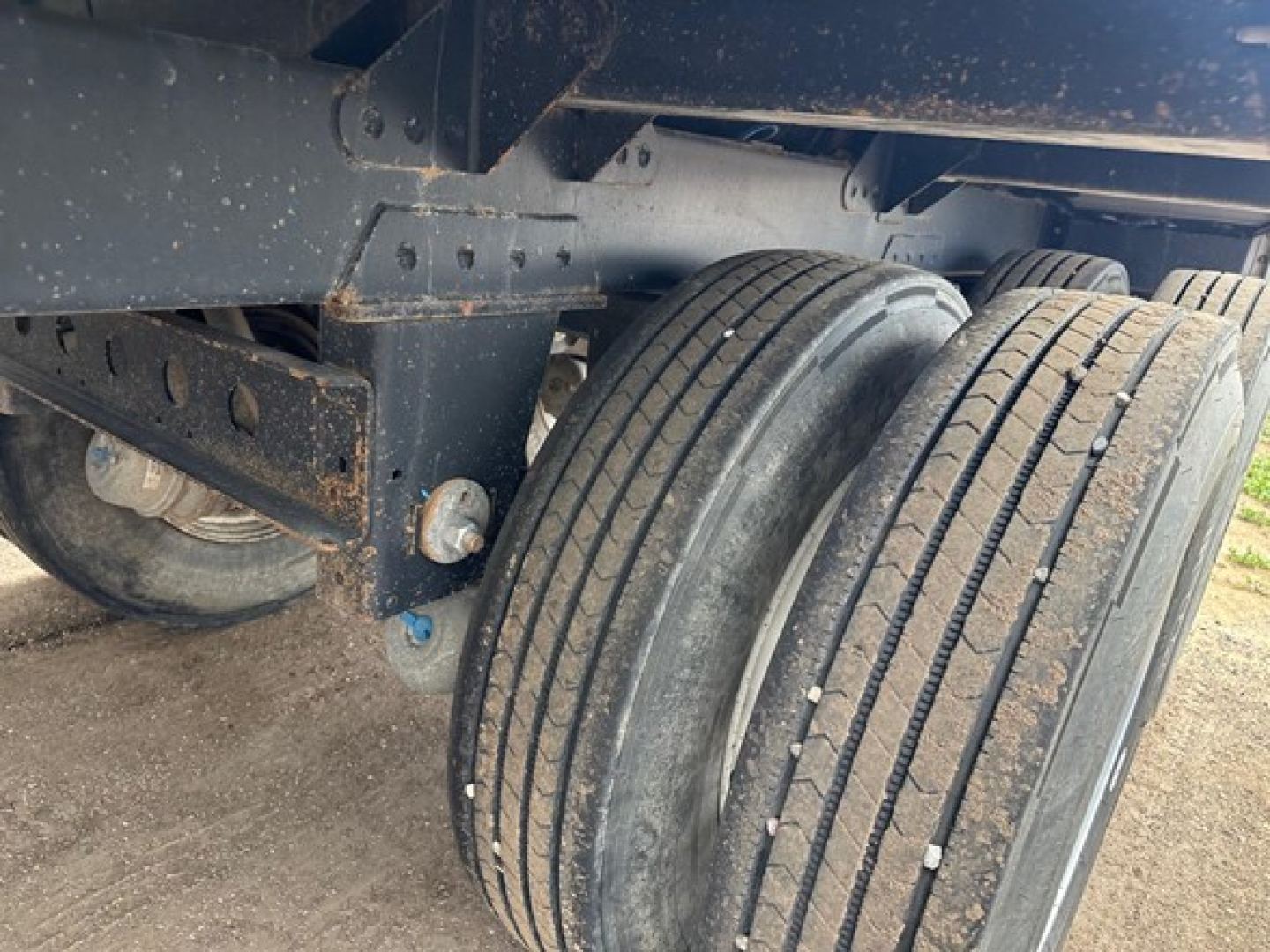 Trailer axle showing dual tires and undercarriage of a hopper trailer with metal frame and suspension components.