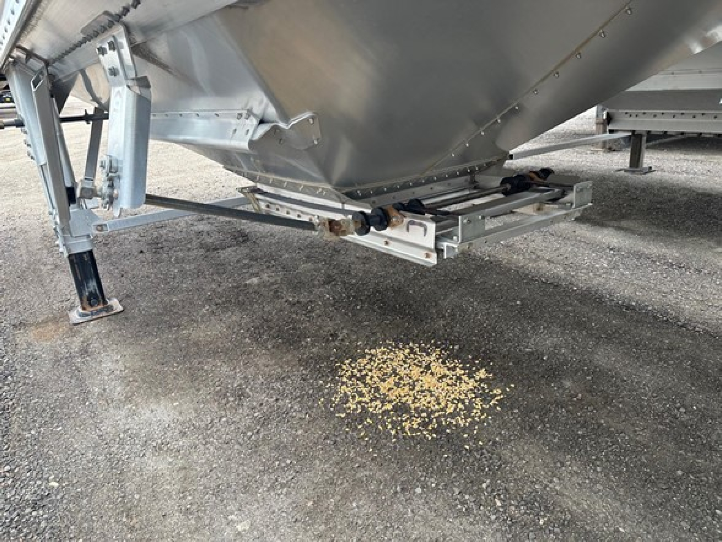 Timpte Super Hopper trailer underside view showing hitch and support structure with scattered corn kernels on ground.