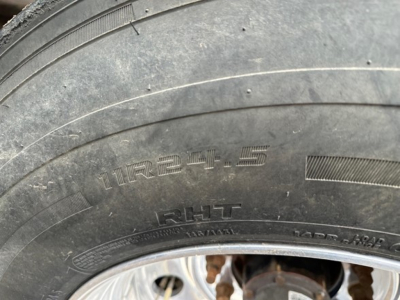 Tire close-up on a 2024 Timpte Super Hopper trailer showing the tire size 11R24.5 and rim hub area with visible rust on undercarriage components.