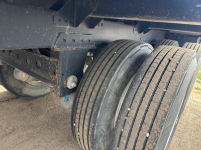 Trailer axle showing dual tires and undercarriage of a hopper trailer with metal frame and suspension components.
