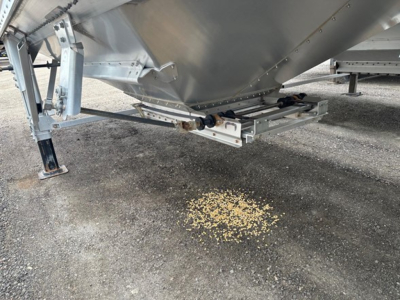 Timpte Super Hopper trailer underside view showing hitch and support structure with scattered corn kernels on ground.