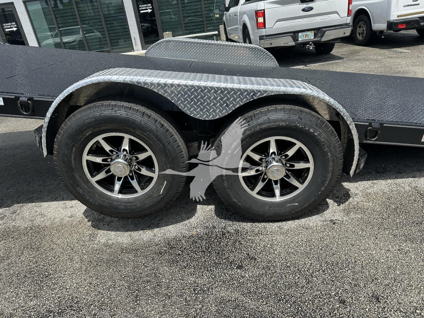 Trailer axle and dual wheels with diamond plate fenders on a flatbed trailer.