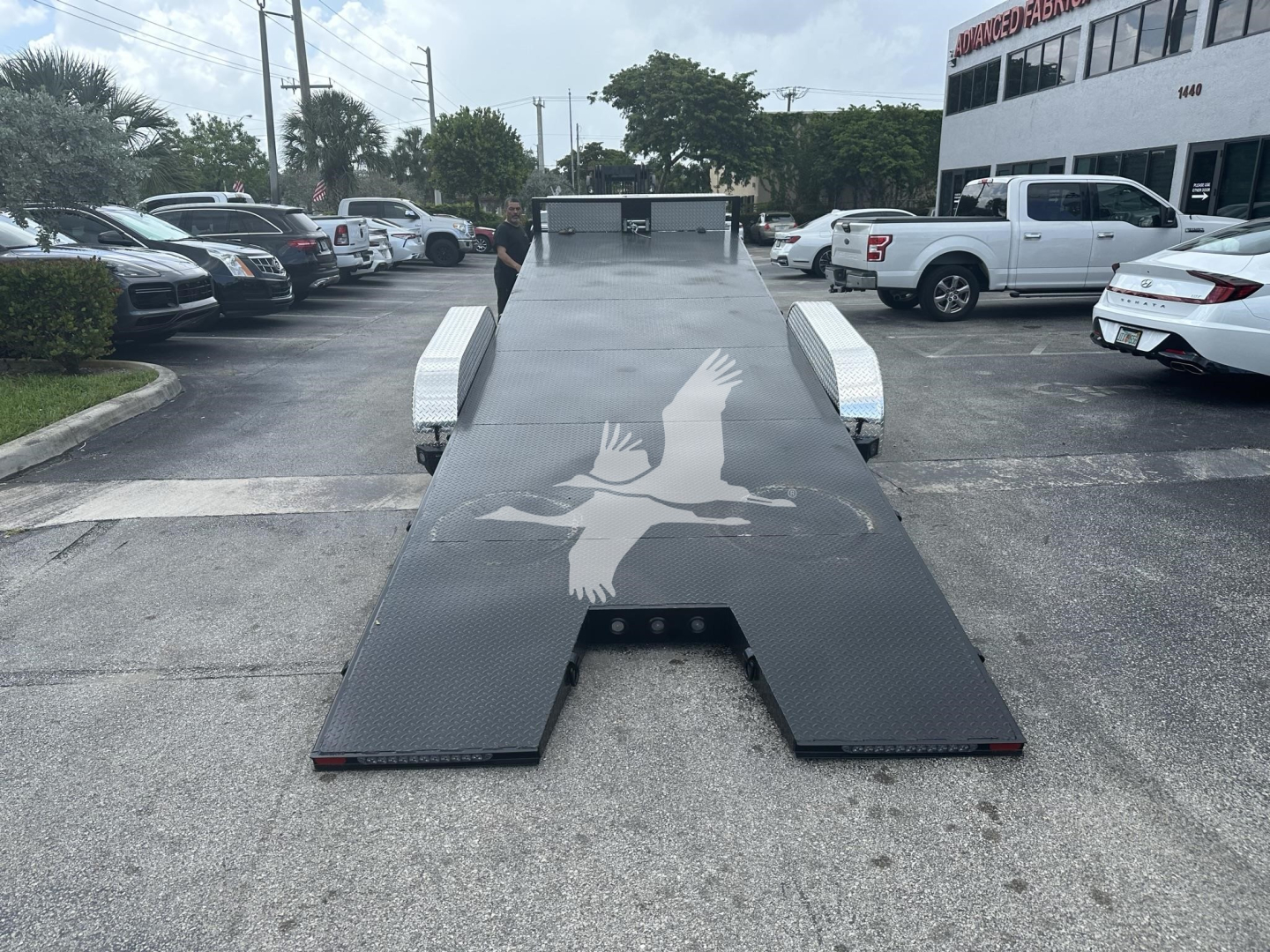 Flatbed trailer with a large white bird graphic on the deck, viewed from the rear, showing steel diamond-plate surface and side ramps.
