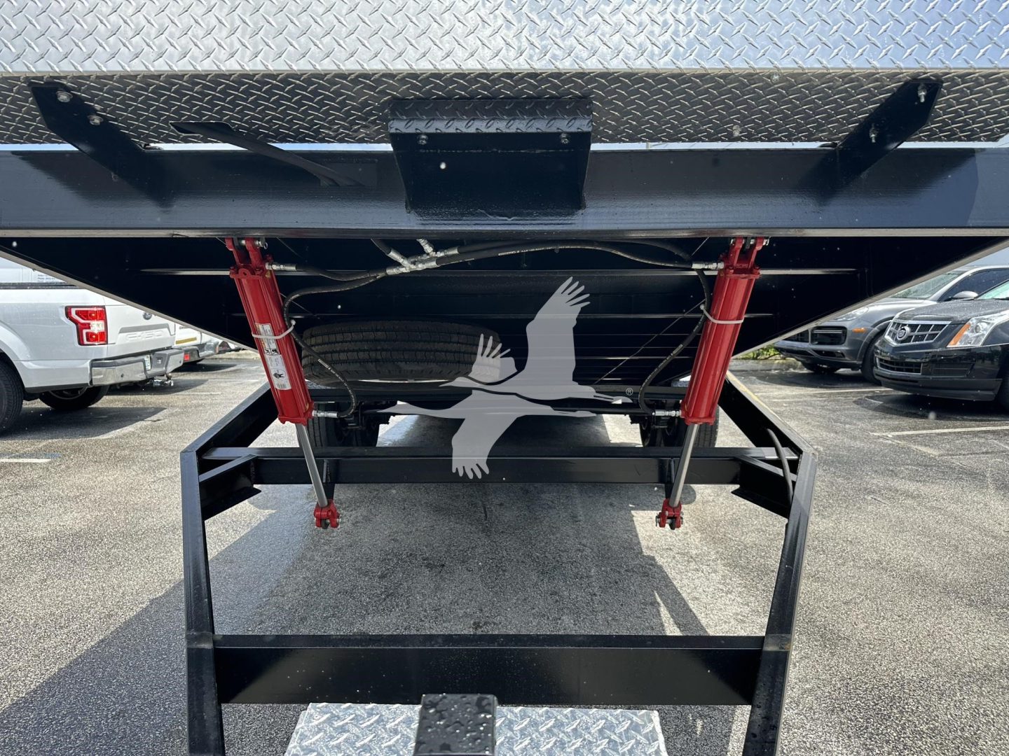Trailer hitch area showing underside of a flatbed trailer with red support brackets and a black step/loader plate, diamond plate top surface visible.