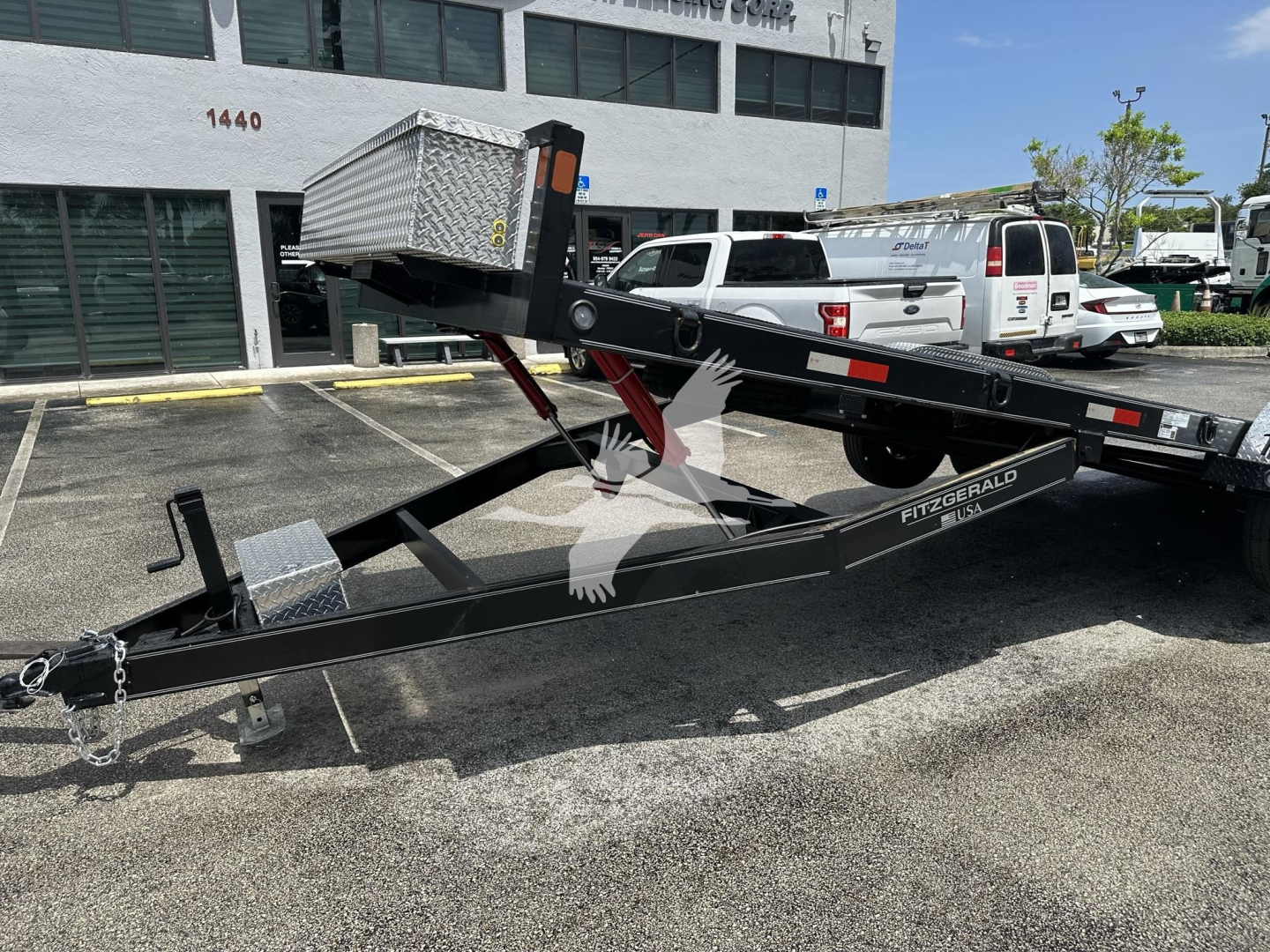 Trailer hitch with a raised toolbox on top, black C-channel frame, front hitch and safety chains, white storage box on top of the trailer bed.