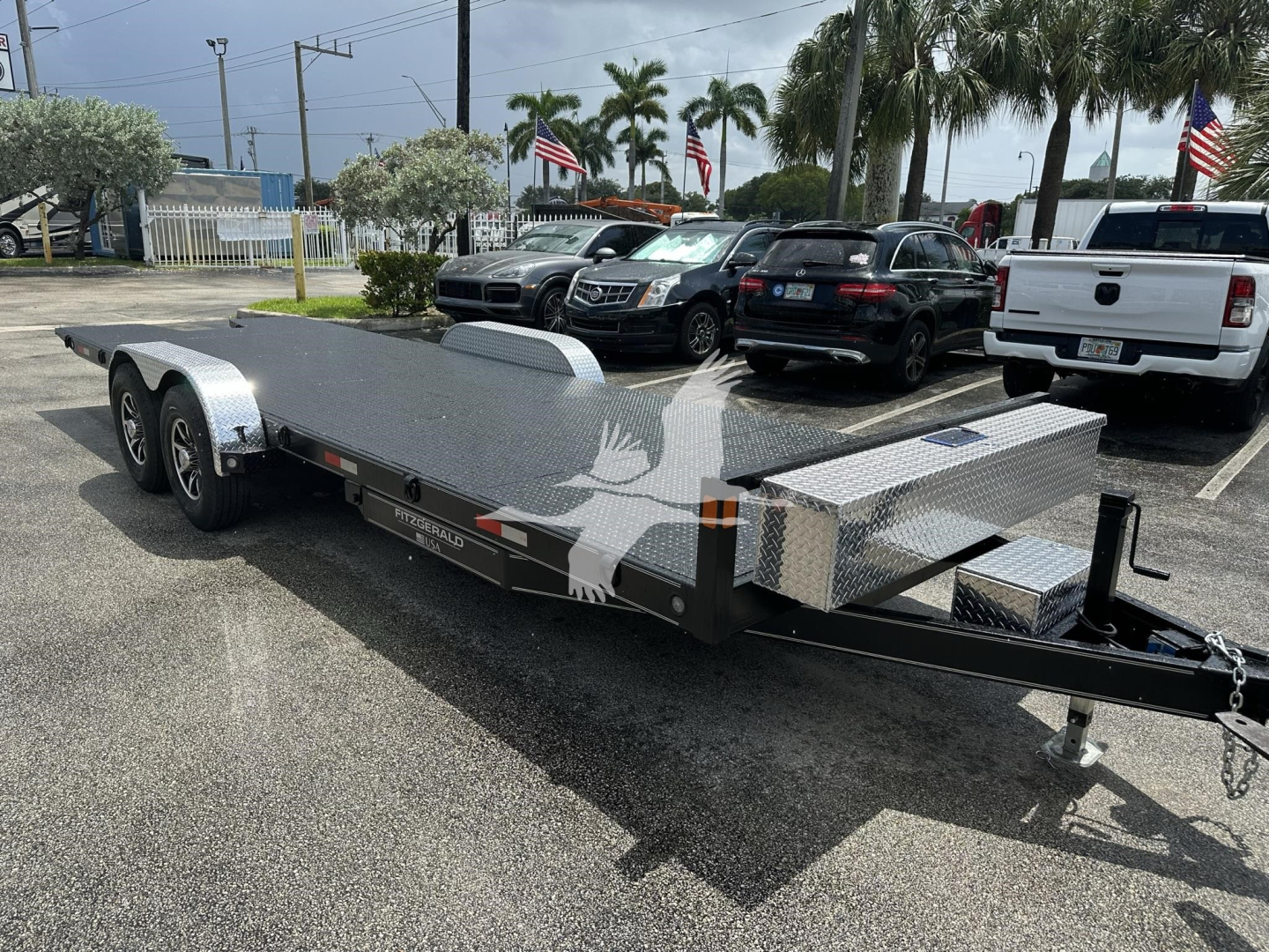 Trailer-style equipment trailer with dual axles and diamond plate ramp in a parking lot.
