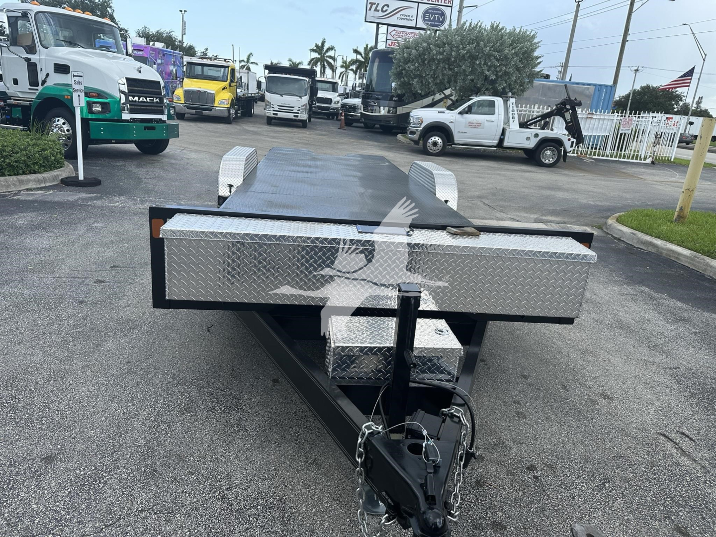 Flatbed trailer hitch on an equipment trailer with diamond plate toolbox and steel rails, viewed from the front in a dealership lot.