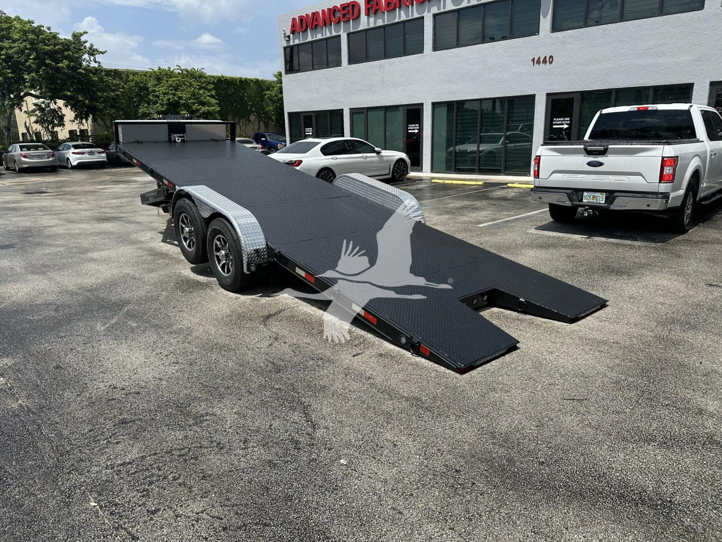 Trailer with ramped deck in a parking lot showing a low-angle view of a flatbed equipment trailer with dual axles and a folding ramp.
