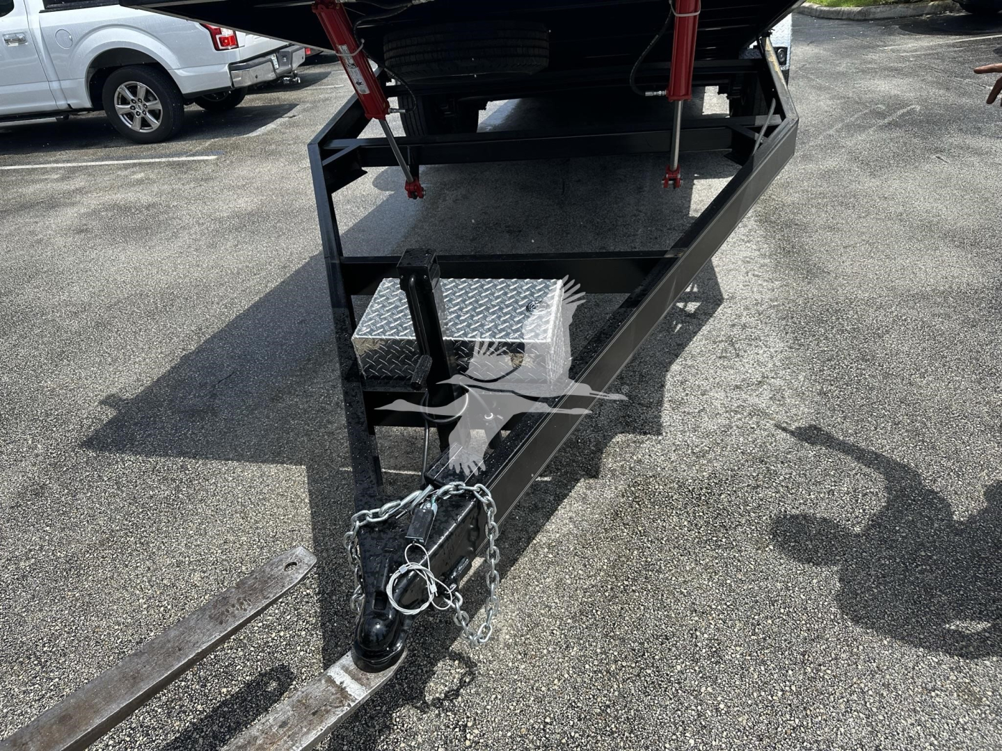 Trailer hitch and front frame of a new trailer showing hitch coupler and safety chains with diamond plate toolbox.