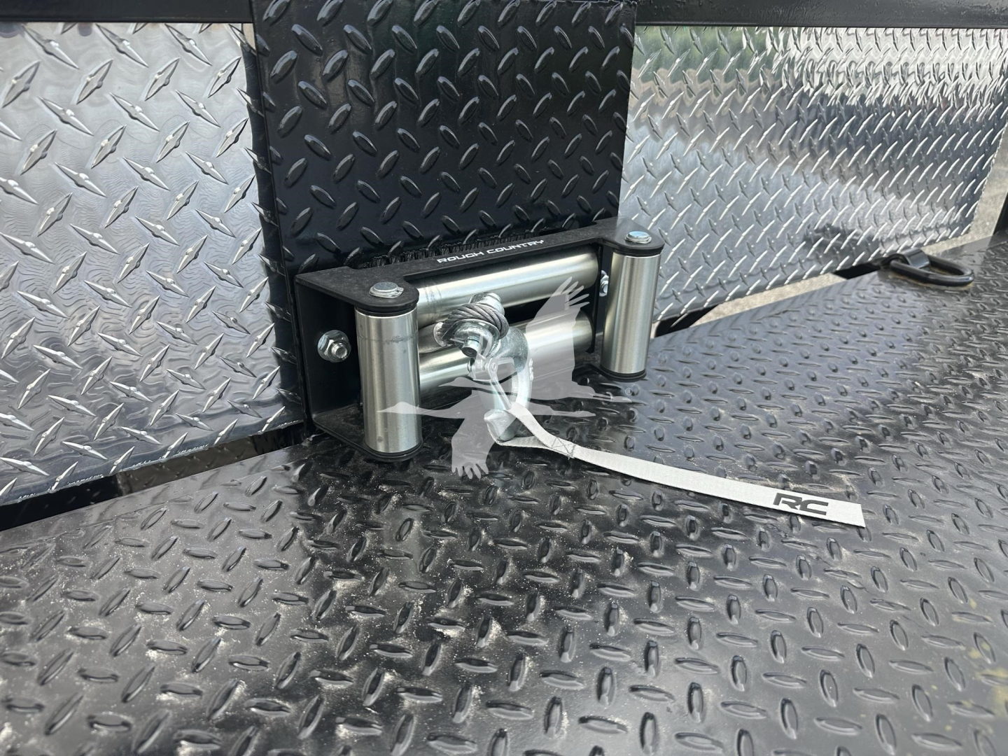 Trailer hitch with coupler and silver diamond-plate exterior, side-mounted mechanism, and tethered tag showing FZTR00733FM on a black textured surface.