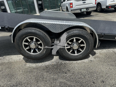 Trailer axle and dual wheels with diamond plate fenders on a flatbed trailer.