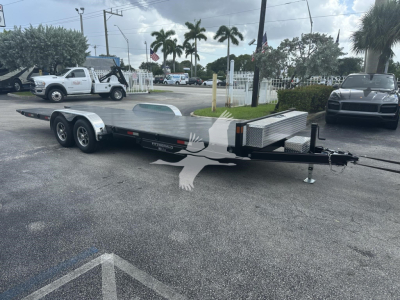 Trailer flatbed with dual-axle, silver finish, 7-foot long bed, gooseneck hitch, aluminum diamond plate toolbox at rear, light duty bumper, parked in lot.