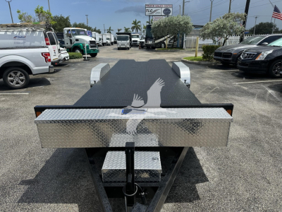 Flatbed trailer with diamond plate tool box at front, ramp deck, and wheel fenders visible; stock number FZTR00733FM in a dealership lot.