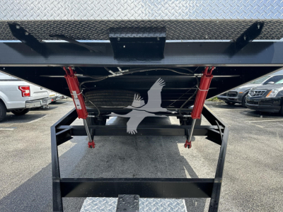 Trailer hitch area showing underside of a flatbed trailer with red support brackets and a black step/loader plate, diamond plate top surface visible.