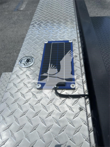 Solar panel and diamond plate trailer step with mounted solar charging panel and cable visible on aluminum deck.