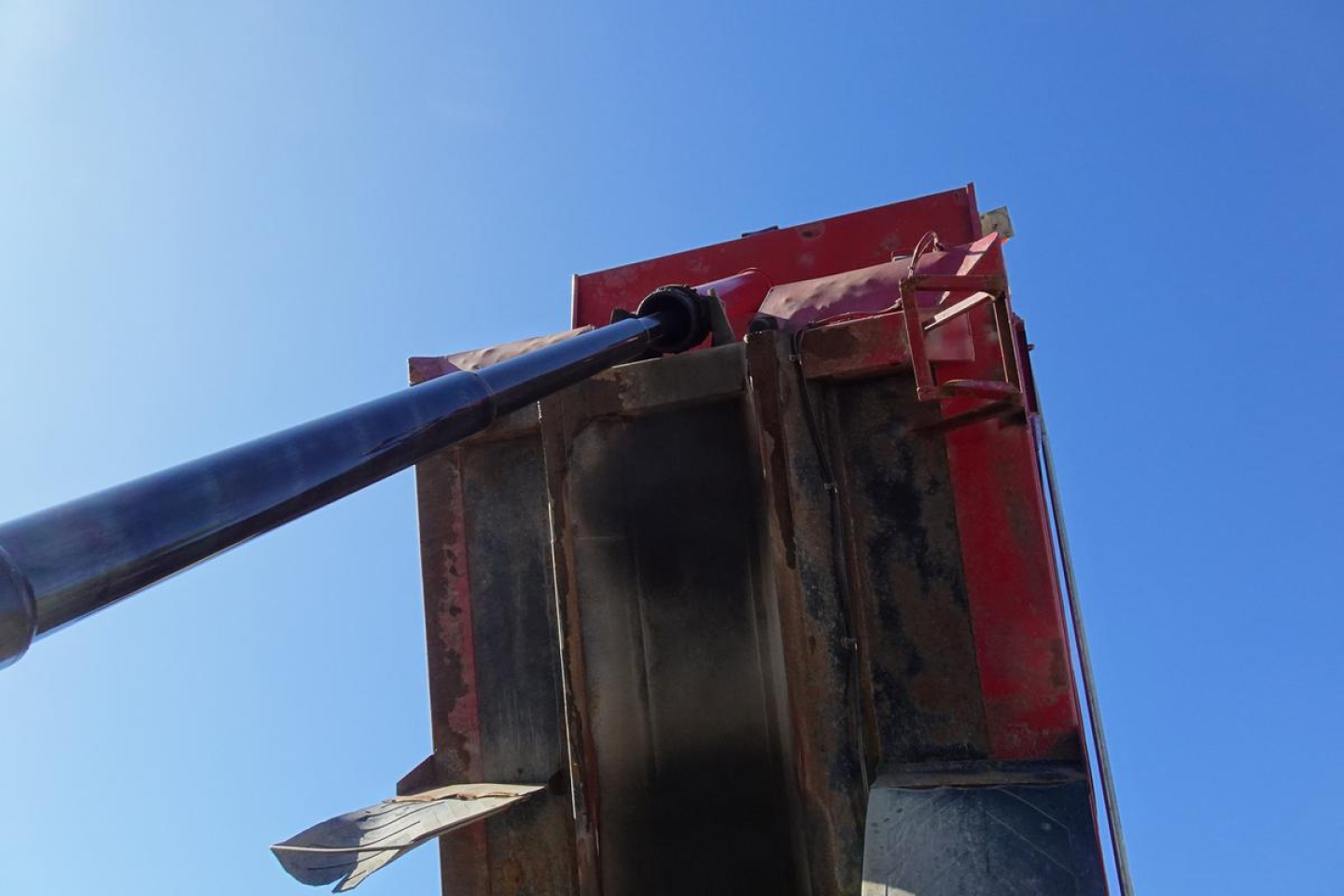 Section of a dump truck bed with hydraulic ram in view, metal structure and red paint visible.