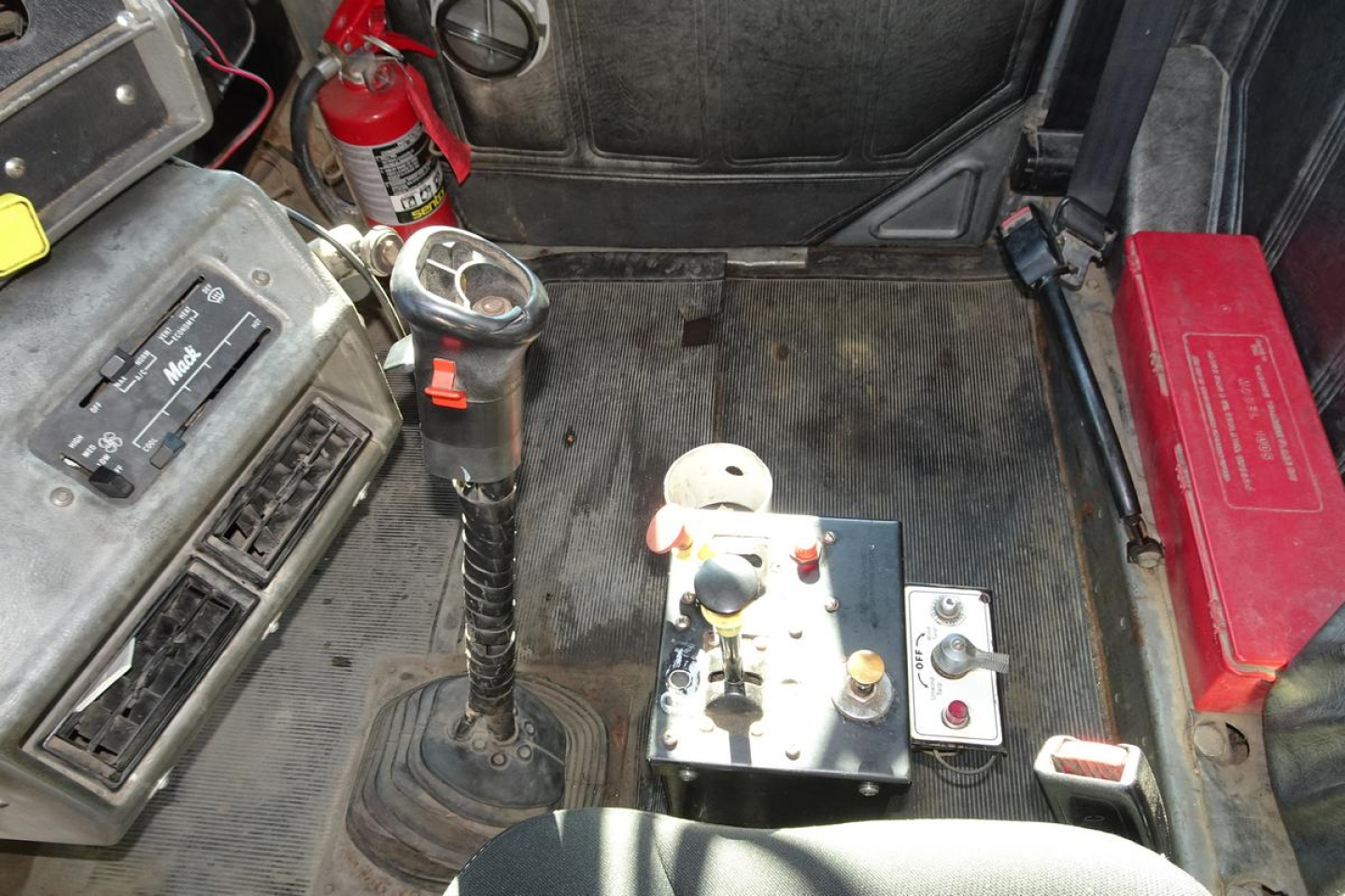 Vehicle interior showing gear shifter, control panel, fire extinguisher, and red battery box in Mack RD RD688S cab; ports and levers visible.