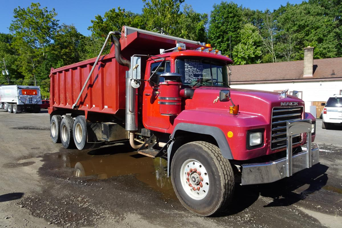 Dump truck chassis and cargo bed visible with red cab and red dump body. Mack RD68S with three rear axles, front grille, and side mirrors.