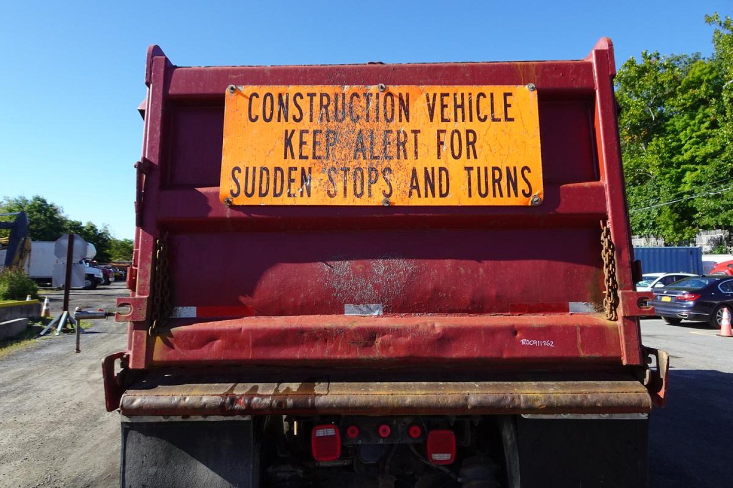 Rear view of a red dump truck with an orange sign reading Construction Vehicle Keep Alert for Sudden Stops and Turns.