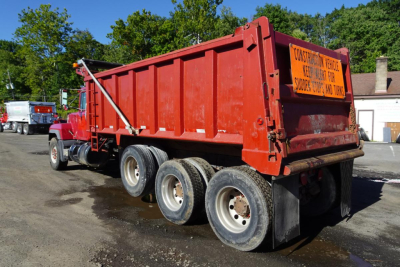 Red Mack RD RD688S dump truck with orange construction sign on the bed showing multiple axles and tires.