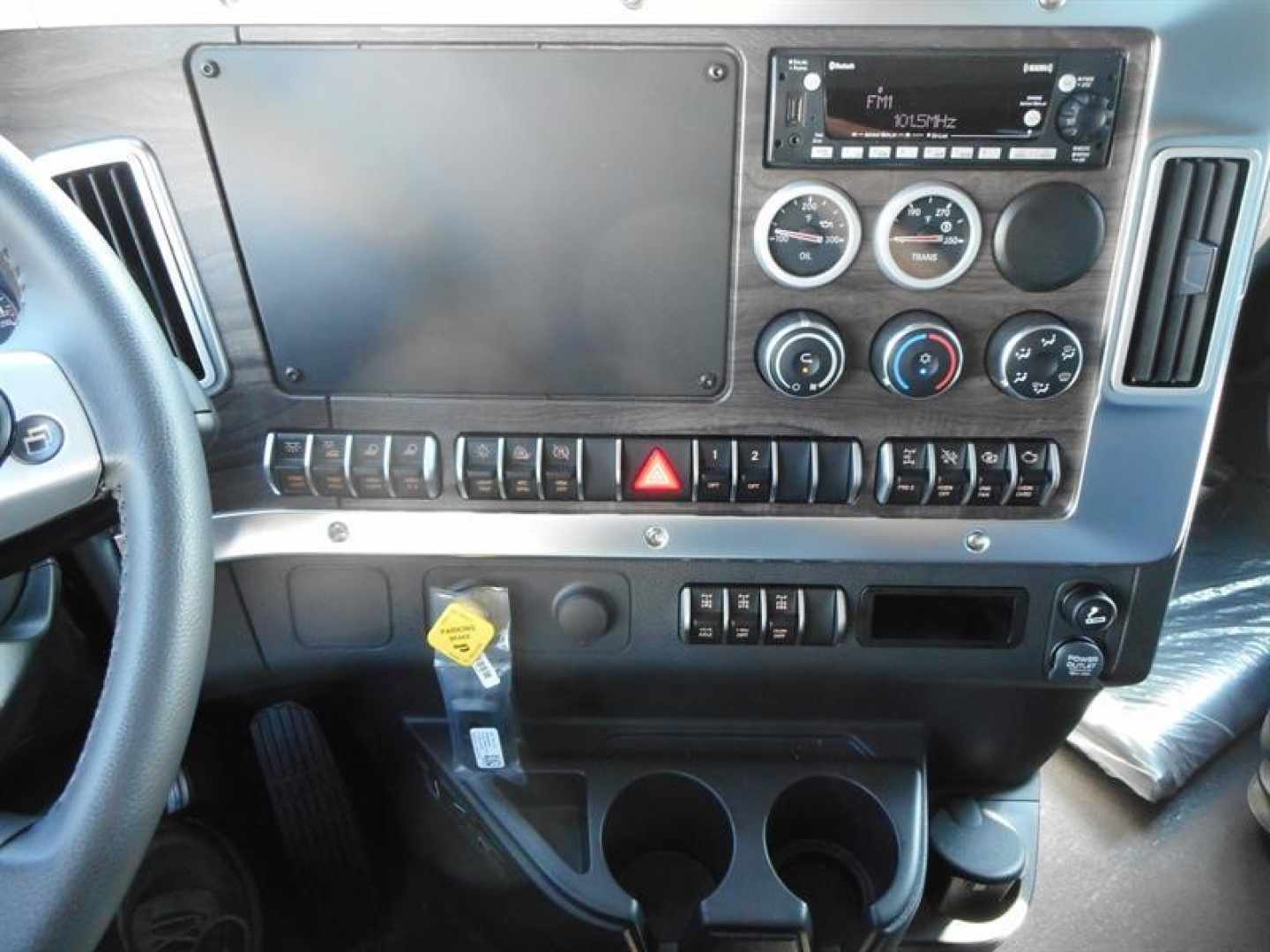 Dashboard interior of a Western Star 47X showing a large blank/covered screen, circular gauges, climate controls, radio unit, hazard button, switch panel, key tag, and cup holders.