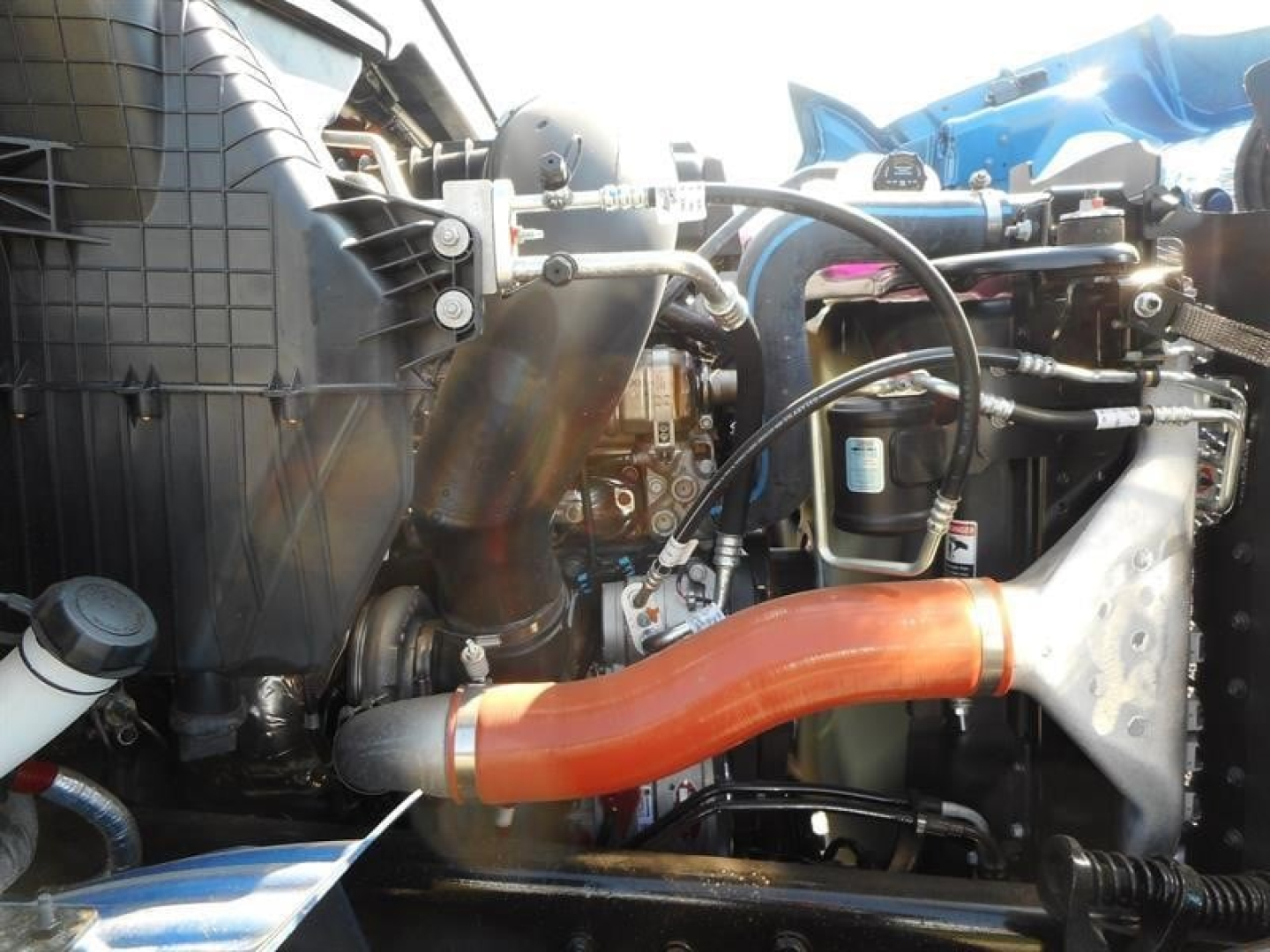 Engine bay of a Western Star 47X showing orange coolant hose, intake components, and hydraulic lines.