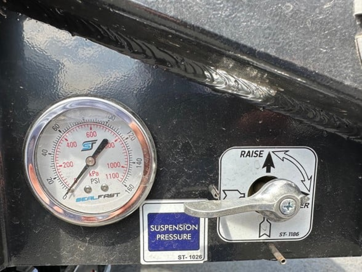 Drop deck trailer gauge showing suspension pressure label and raise lever.