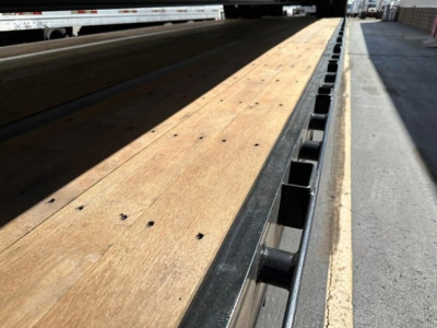 Trailer loading deck showing wooden floor with nail holes and black steel edge rails, beavertail style on a drop deck trailer.