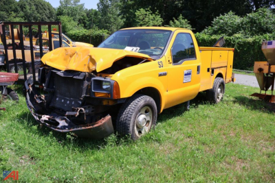 Front-left view of a damaged yellow 2005 Ford F-350 Super Duty utility truck with a crumpled hood and front bumper, utility bed, in a grassy lot.