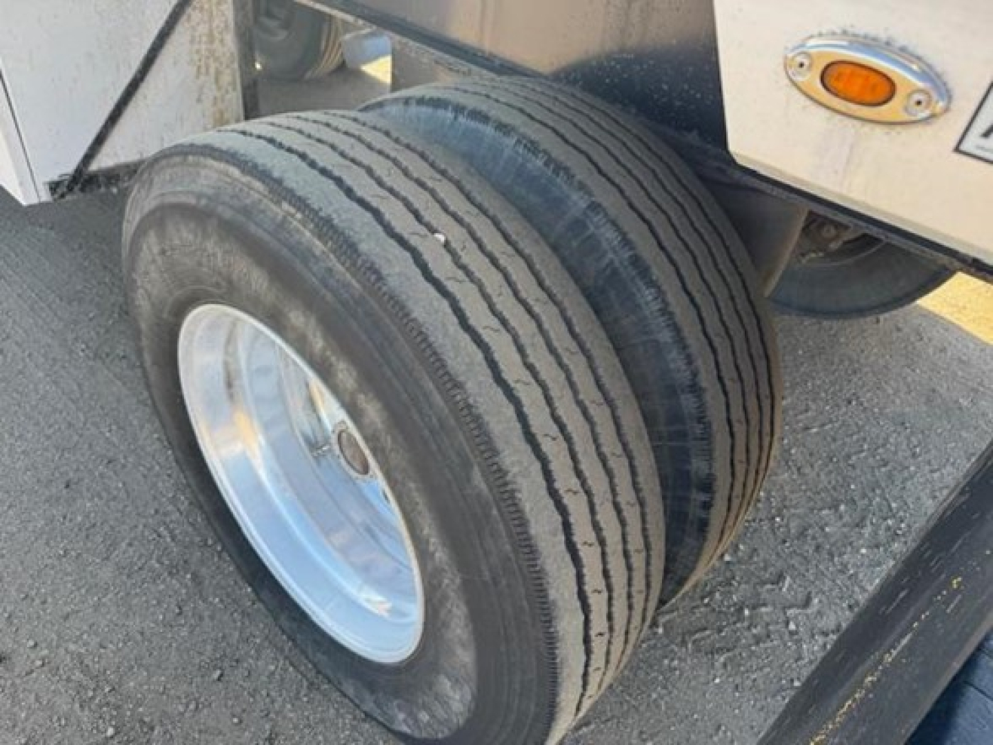 Trailer wheel close-up showing dual rear tires and white rim on Utility 4000Ae flatbed trailer.