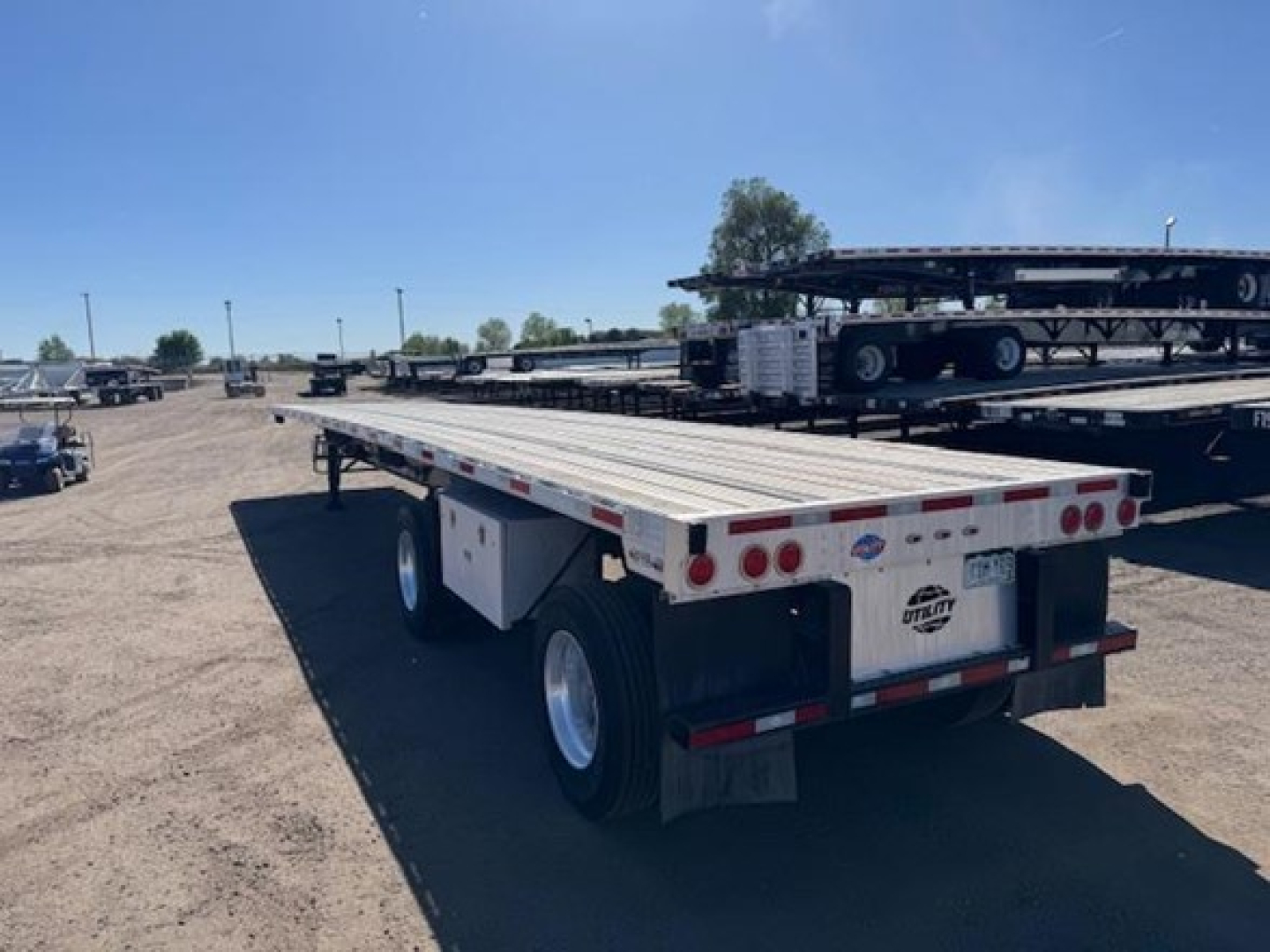 Utility flatbed trailer showing flatbed deck and rear lights with dual axle configuration, license plate area, and rear underride bumper.