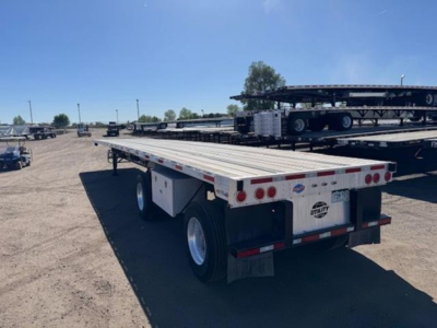 Utility flatbed trailer showing flatbed deck and rear lights with dual axle configuration, license plate area, and rear underride bumper.