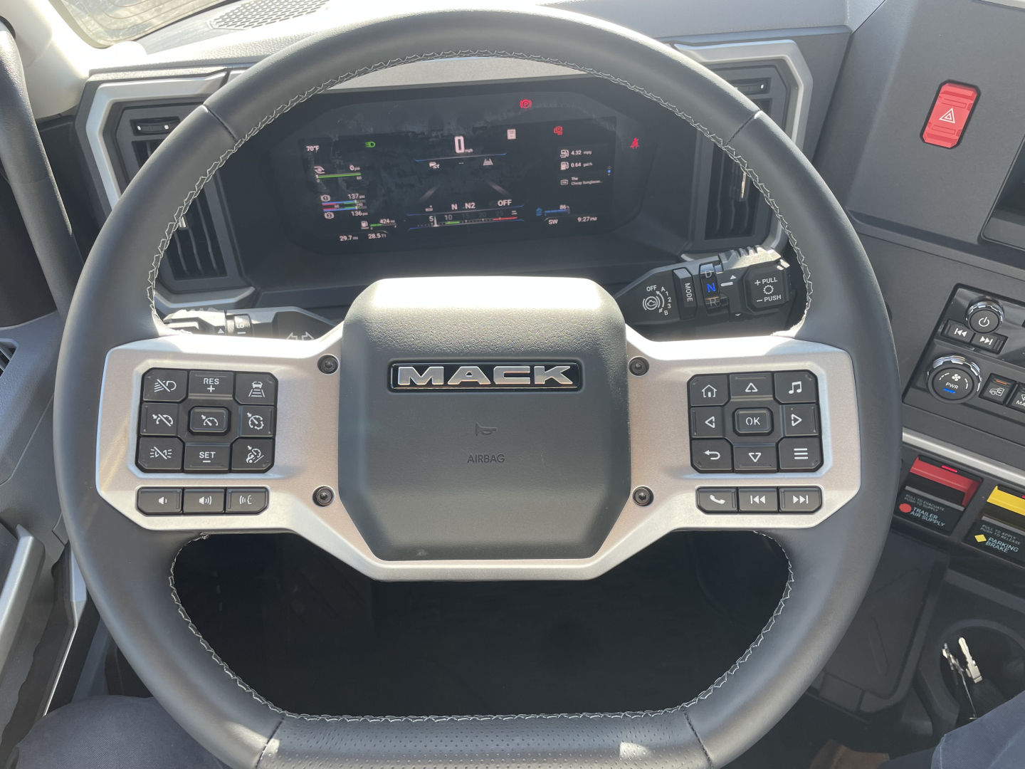 Mack PR64T truck cabin interior showing steering wheel with Mack logo and dashboard display.