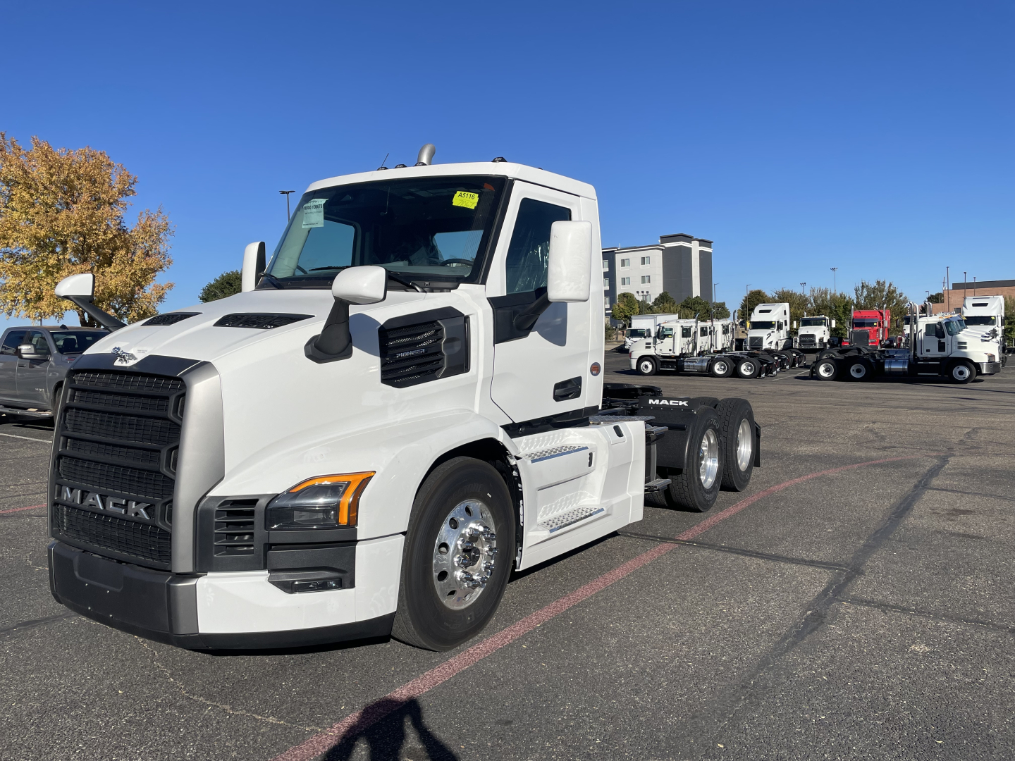 Mack PR64T conventional daycab truck in a dealership lot, white cab, 3-axle tractor with sleeperless design.