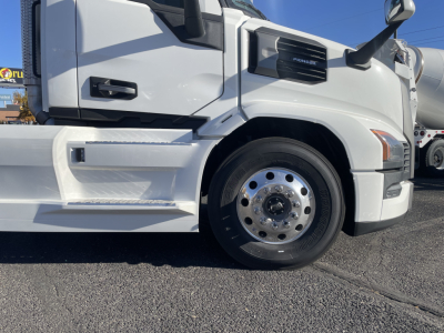 Front half of a white Mack PR64T truck showing front wheel, fender, and cab with step; visible badge and side mirror.