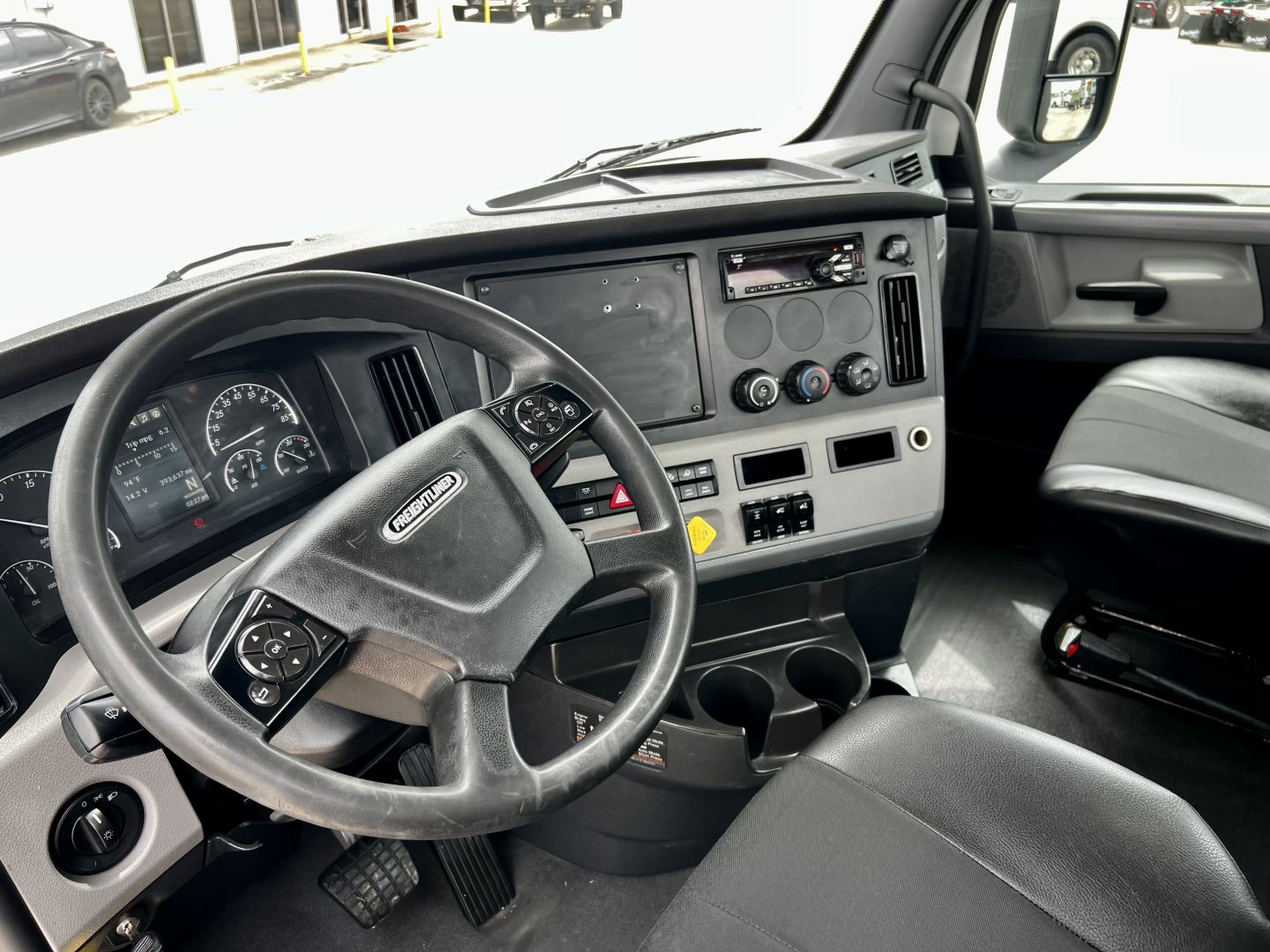 Cab interior of a 2020 Freightliner Cascadia 126 showing steering wheel, gauge cluster, center console with cup holders and controls, and driver seat.