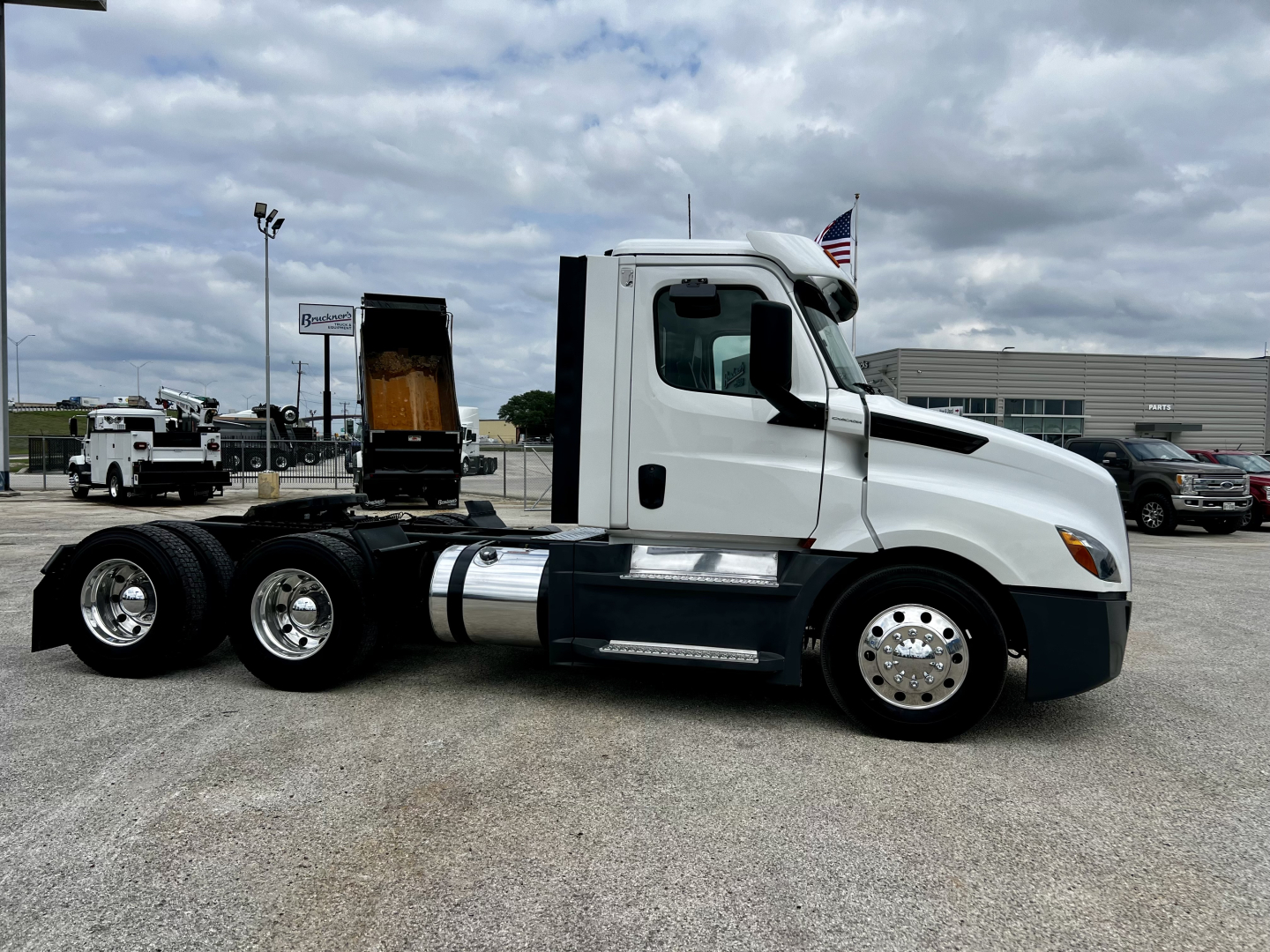 Truck side view of a 2020 Freightliner Cascadia 126 daycab, white exterior, dual rear axles, fuel tanks, chrome wheels, and a raised sleeper undercarriage area visible.