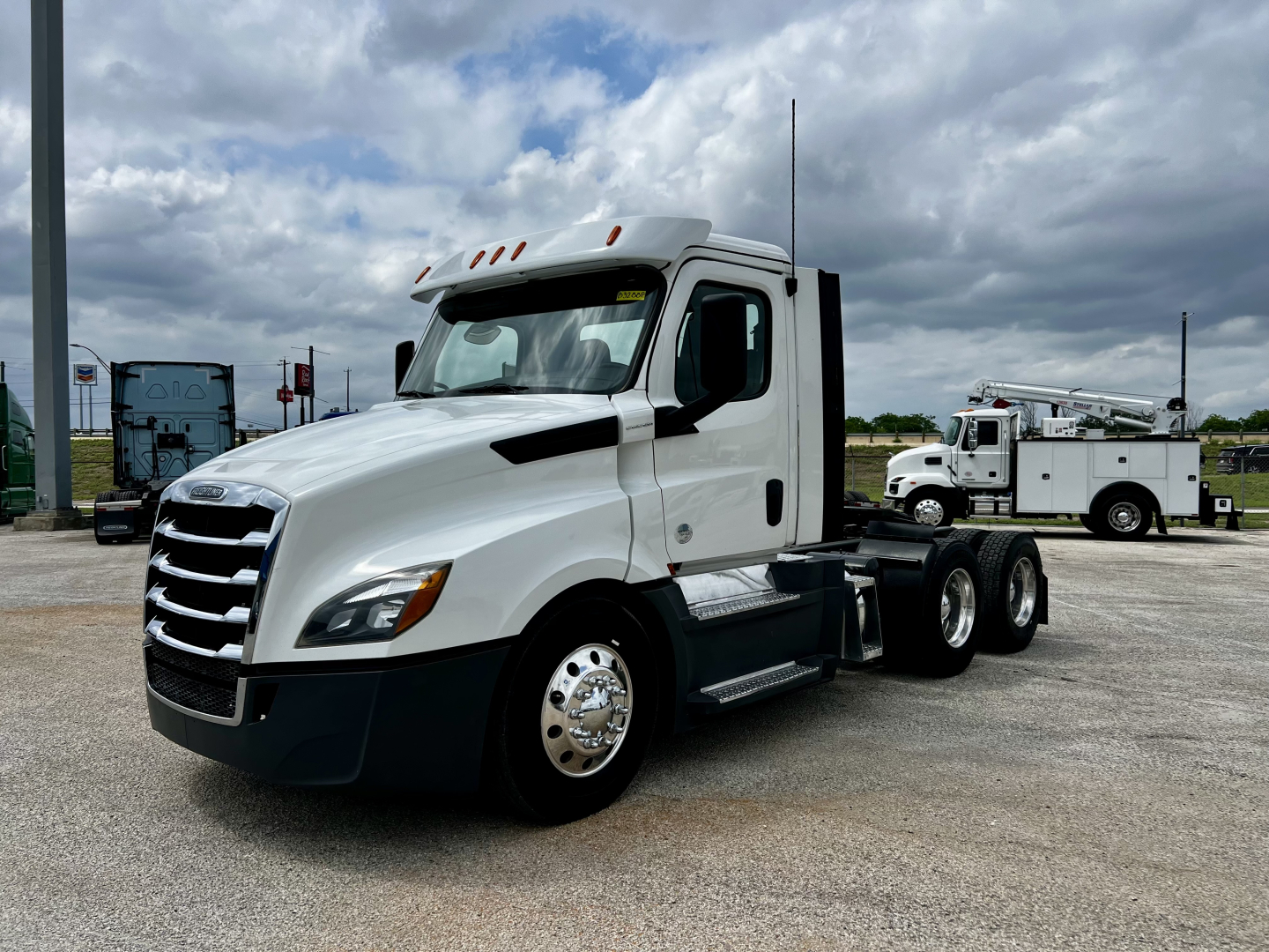 Freightliner Cascadia 126 daycab truck in a lot, front three-quarter view showing white cab, black bumper, and dual rear axles.