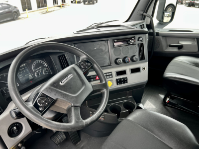 Cab interior of a 2020 Freightliner Cascadia 126 showing steering wheel, gauge cluster, center console with cup holders and controls, and driver seat.