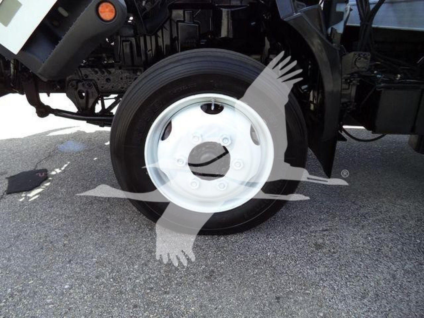 Front wheel and suspension of a refrigerated truck showing a white steel wheel and tire, partial chassis, no legible text visible