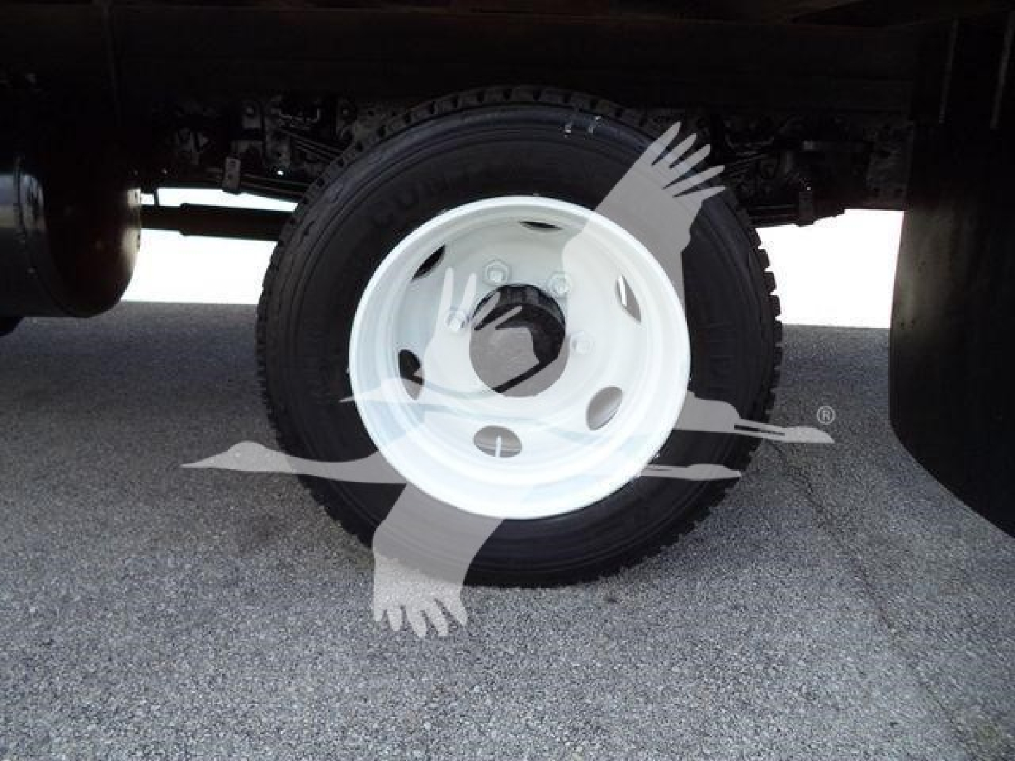 Wheel and tire under a refrigerated truck chassis showing white steel rim and tire sidewall.