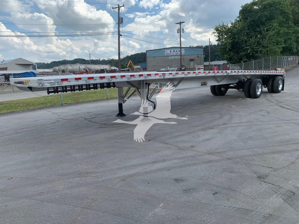 Flatbed trailer with low-profile deck showing tandem axles and landing gear.