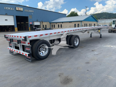 Flatbed trailer showing dual axles with chrome wheels and red/white reflective tape along the sides in a dealership lot.