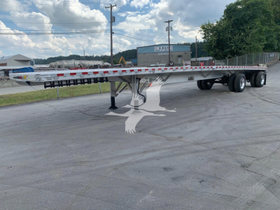 Flatbed trailer with low-profile deck showing tandem axles and landing gear.