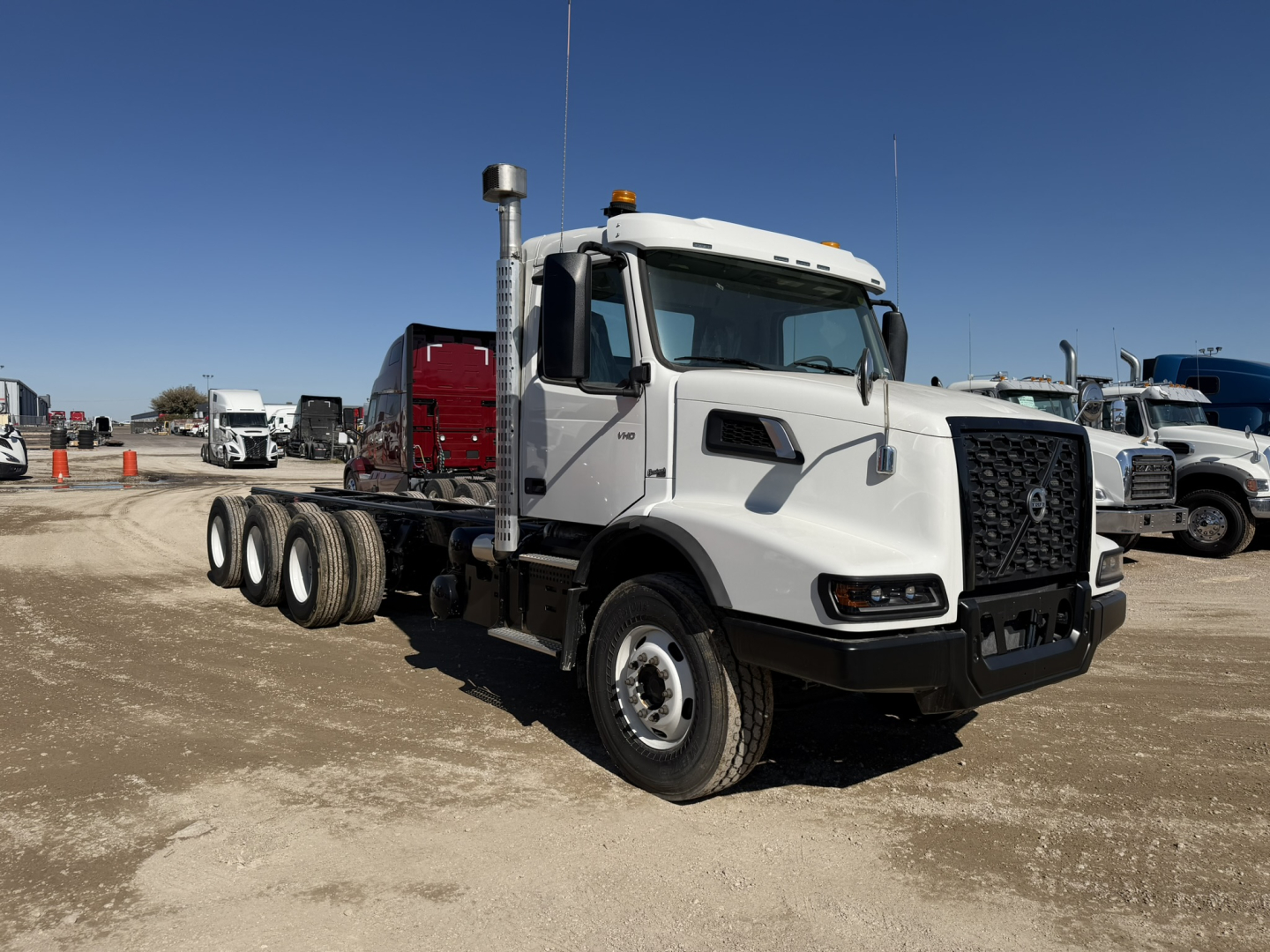 Volvo VHD86B300 cab and chassis truck with white cab and black grille, dual rear axles, on a dirt lot.