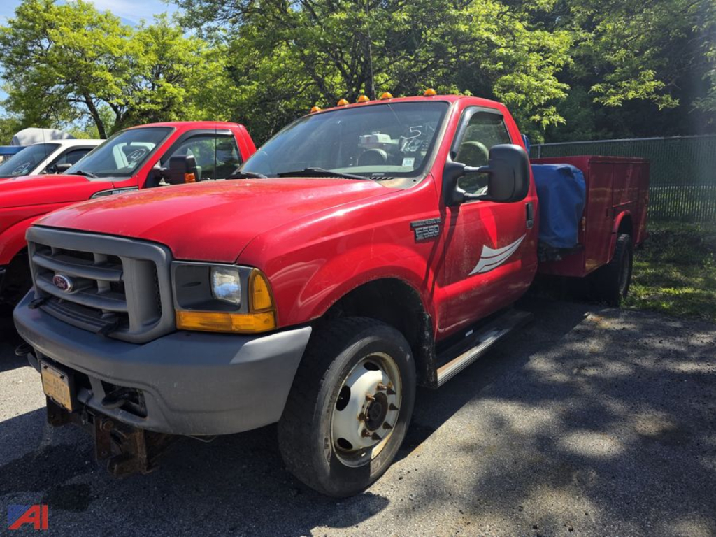 Red 2001 Ford F-550 Super Duty utility truck in a parking lot, front-left view with black grille, gray bumper, single cab, utility bed behind cab, other red trucks in background.