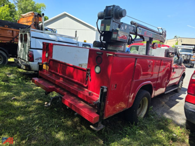 Ford F-550 Super Duty utility truck with mounted crane in red service bed, rear view showing tool compartments and spare tires.